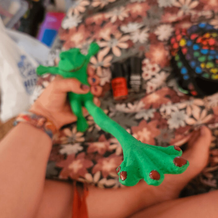 Green DIY frog project with painted details, held in hand over a floral background.