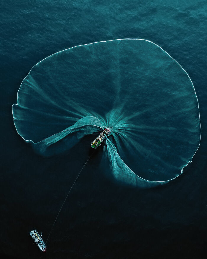 Aerial view of a fishing boat with a large net in the ocean, showcasing a stunning nature photograph.