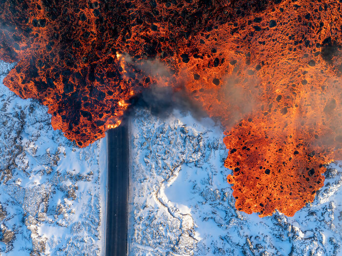 Aerial view of a lava flow crossing a snowy road, showcasing nature's contrast and power. Aerial view of a lava flow crossing a snowy road, showcasing nature's contrast and power.