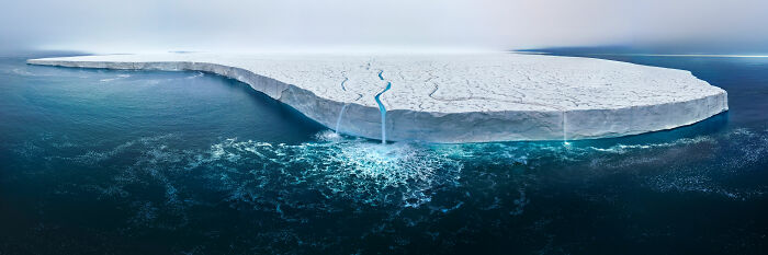 Award-winning nature photo of a large iceberg with meltwater flowing into the ocean, showcasing stunning natural beauty.