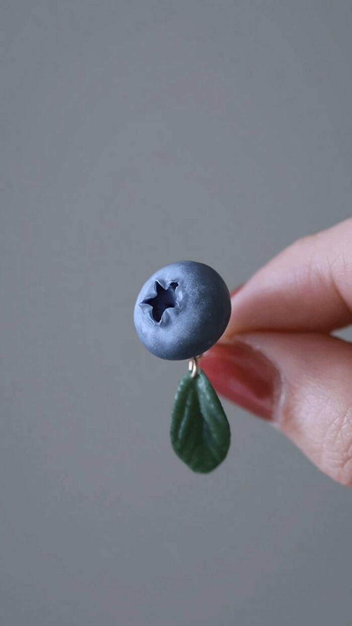 A hand holding a DIY blueberry craft with a small leaf attached.
