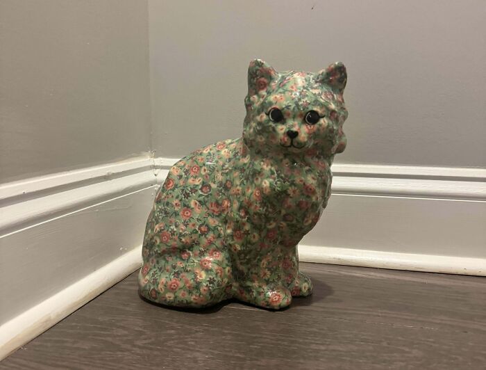 Floral ceramic cat sculpture found while thrifting, placed in a room corner with gray walls and wooden flooring.