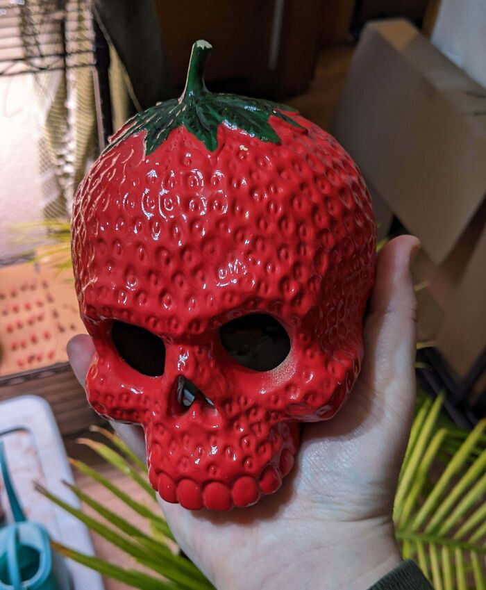 A hand holds a ceramic skull designed as a strawberry, showcasing an unexpected thrift find treasure.