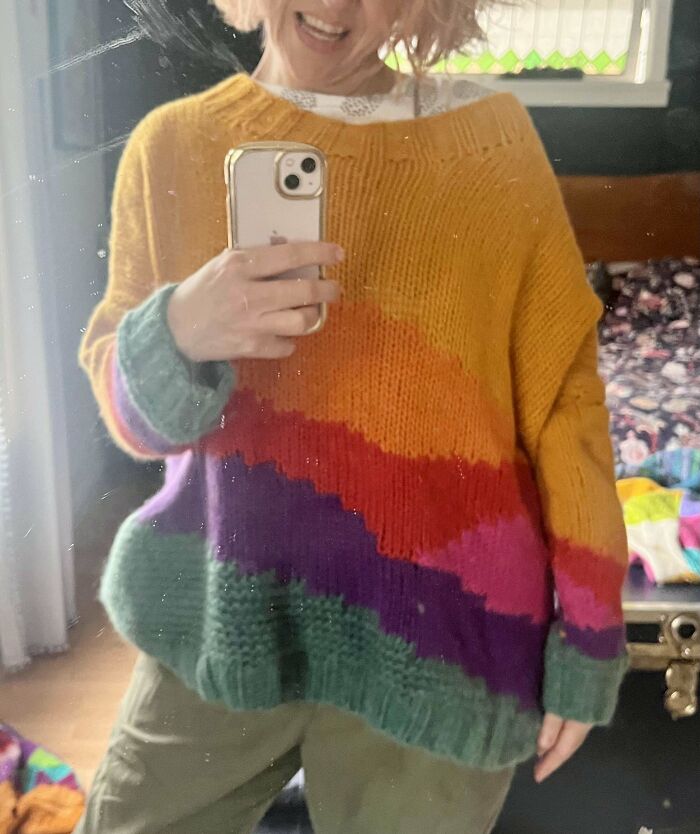 Person taking a mirror selfie wearing a colorful thrift store sweater, showcasing unique thrift store finds.