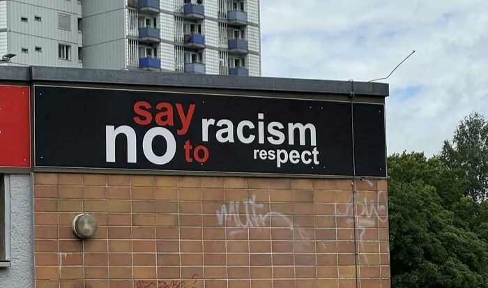 Sign fail with mixed message reading 'say no to racism respect' on a brick wall.