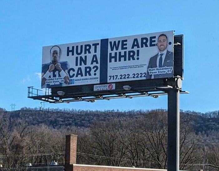 Billboard sign fail: "Hurt in a car? We are HHR!" featuring two individuals with a backdrop of hills and trees.