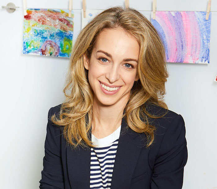 Parenting expert smiling in a casual setting with children's art in the background. Parenting expert smiling in a casual setting with children's art in the background.