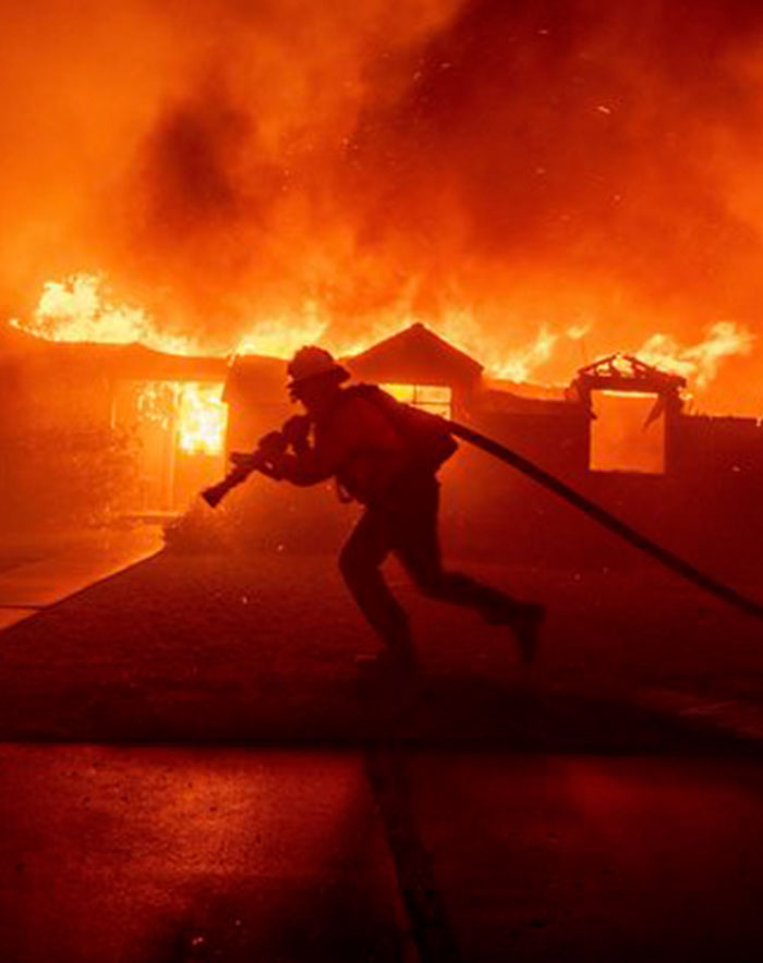 Firefighter battling intense flames with hose amidst a house fire at night. Firefighter battling intense flames with hose amidst a house fire at night.