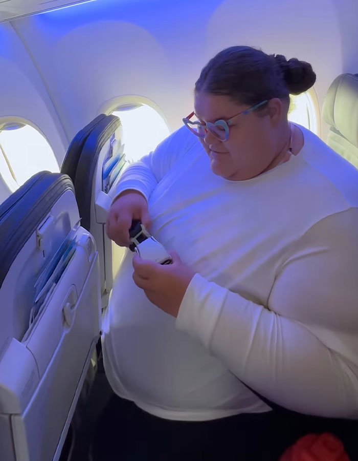 Passenger on a flight adjusting seatbelt, highlighting the debate on airline discrimination against obese passengers. Passenger on a flight adjusting seatbelt, highlighting the debate on airline discrimination against obese passengers.