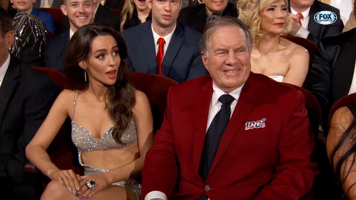Bill Belichick sitting with a woman at an event, both in formal attire, with a crowd in the background. Bill Belichick sitting with a woman at an event, both in formal attire, with a crowd in the background.