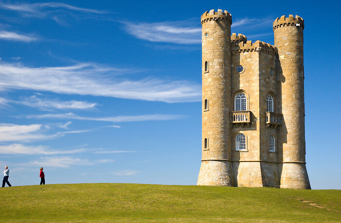Two people walking by a historic, beautiful yet useless building on a hill under a clear blue sky.