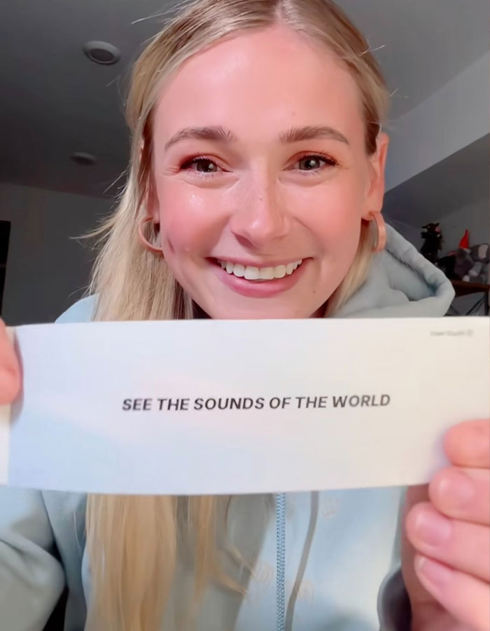 Smiling woman holding a card that reads "SEE THE SOUNDS OF THE WORLD. Smiling woman holding a card that reads "SEE THE SOUNDS OF THE WORLD.