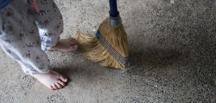 Bare feet near a broom on a concrete floor, illustrating superstition about sweeping feet and marriage concerns.