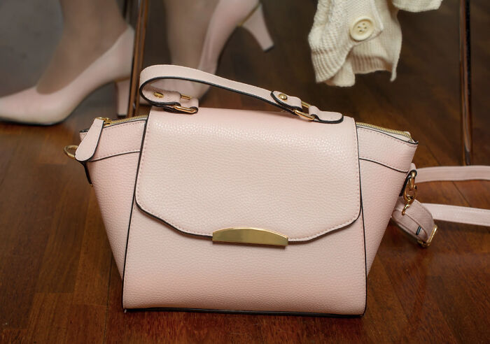 A pink handbag on a wooden floor, related to superstitions about placing bags on the ground.
