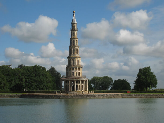 Beautiful useless building by a lake with a cloudy sky backdrop.