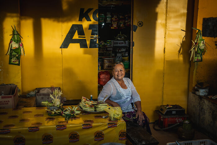 Woman in a traditional outfit preparing for Galungan, Bali, with yellow decorations in the background.