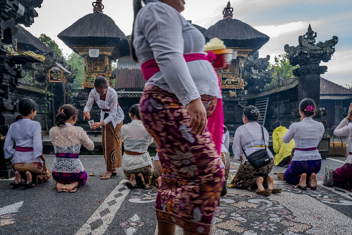 Women in traditional attire kneeling in a Balinese temple during Galungan celebration.