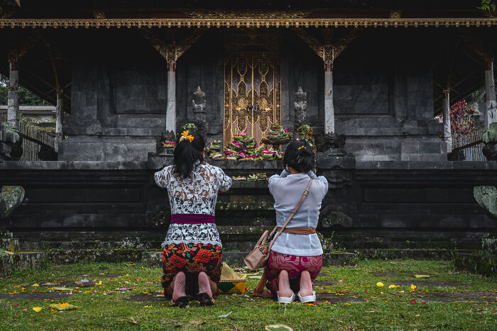 Two women kneeling in prayer during Bali’s Galungan celebration at a temple.