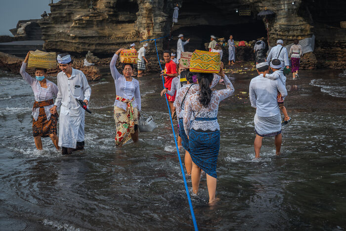 People in traditional attire carrying offerings during Bali’s Galungan celebration by the sea.