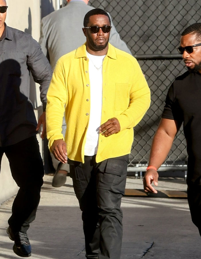 Man in yellow jacket and sunglasses walking with others, related to lawyer quitting as trial approaches. Man in yellow jacket and sunglasses walking with others, related to lawyer quitting as trial approaches.