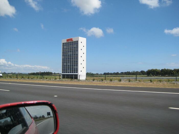 A tall, narrow, roadside motel building stands alone, embodying "beautiful useless buildings" against a clear blue sky.