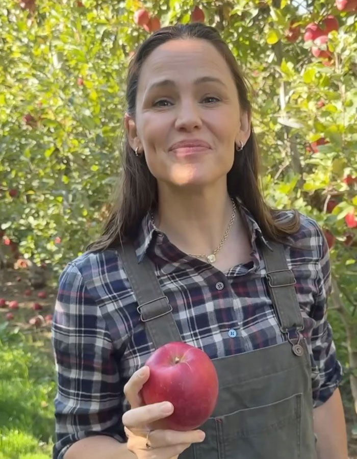 Woman in a plaid shirt outdoors holding an apple, smiling. Woman in a plaid shirt outdoors holding an apple, smiling.