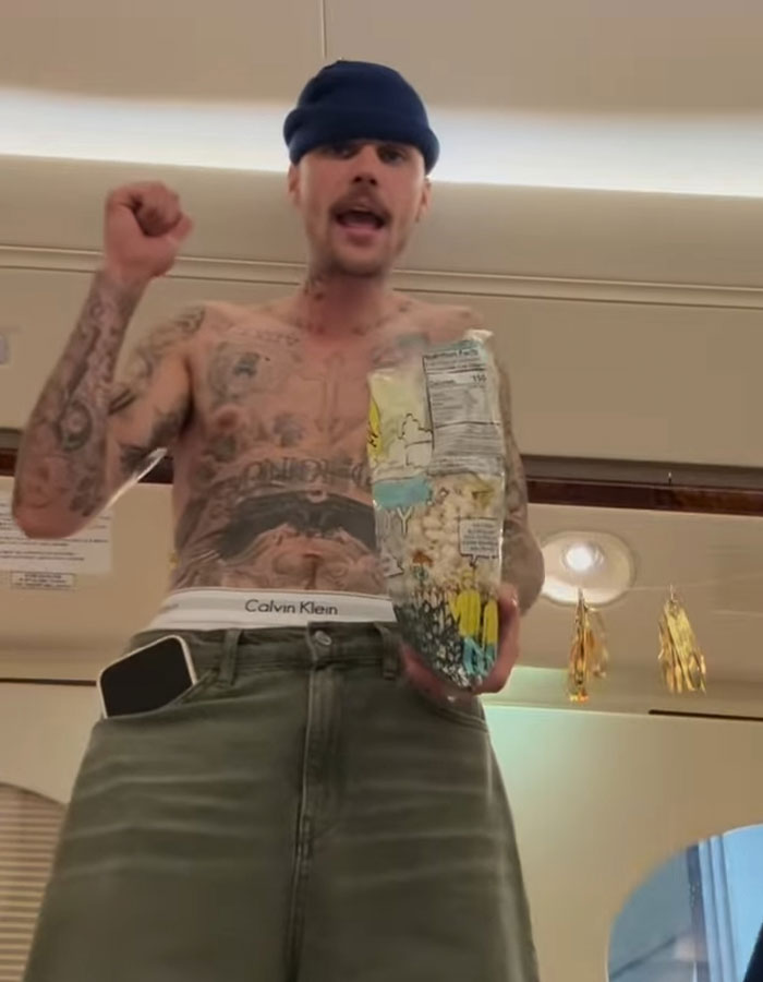 Shirtless man with tattoos holding popcorn in casual setting, wearing beanie and shorts. Shirtless man with tattoos holding popcorn in casual setting, wearing beanie and shorts.