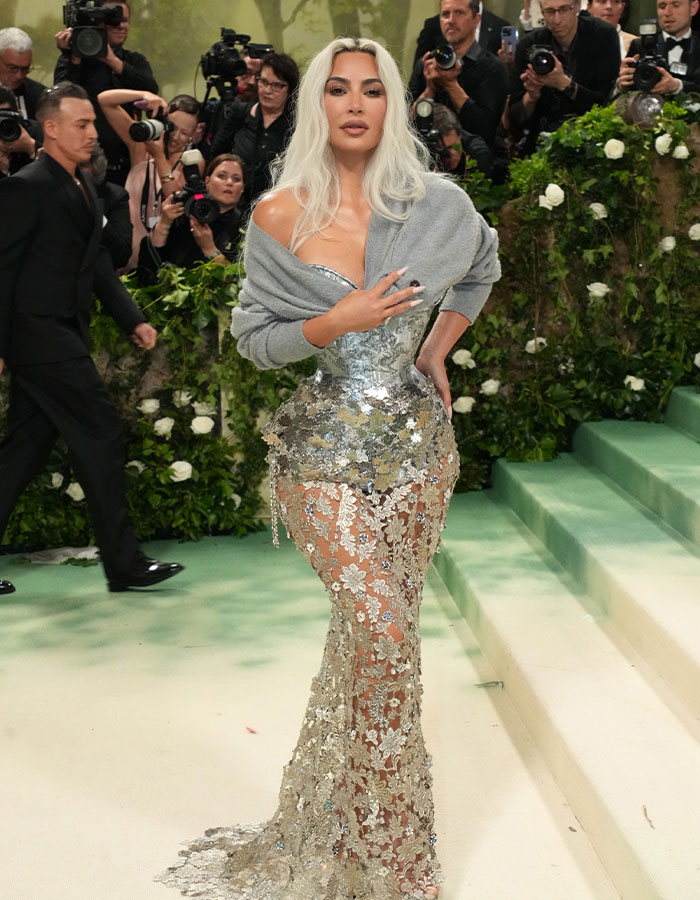 Kim Kardashian at the Met Gala in a tight, shimmering corset dress, surrounded by photographers. Kim Kardashian at the Met Gala in a tight, shimmering corset dress, surrounded by photographers.