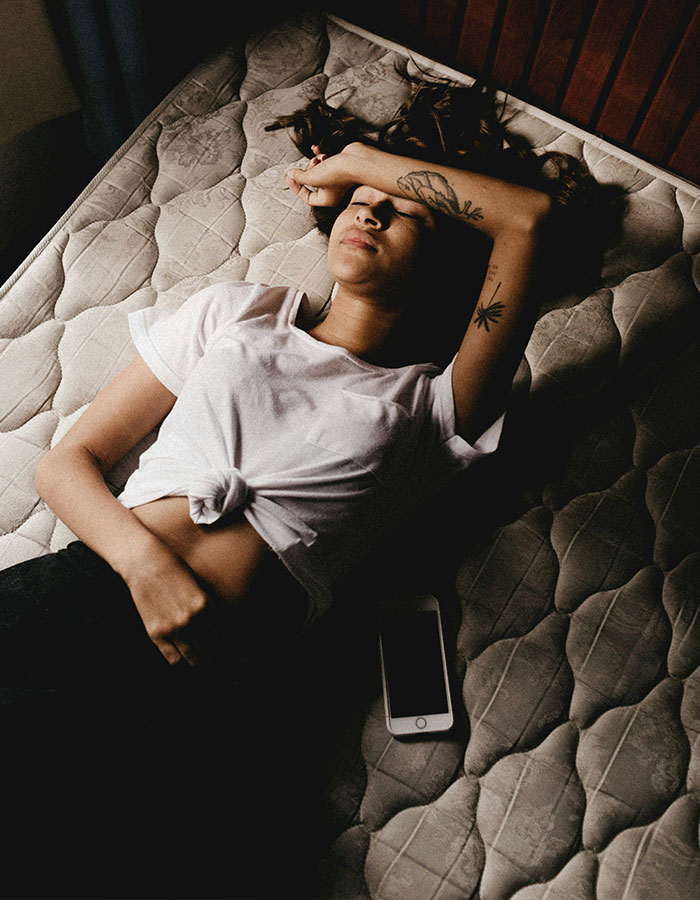 Woman lying on a mattress, phone nearby, reflecting period tracker debate in mobile game context. Woman lying on a mattress, phone nearby, reflecting period tracker debate in mobile game context.