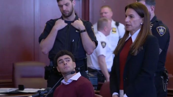 Luigi Mangione's court statement, surrounded by officials, as a woman in a red sweater speaks, gaining public reactions. Luigi Mangione's court statement, surrounded by officials, as a woman in a red sweater speaks, gaining public reactions.