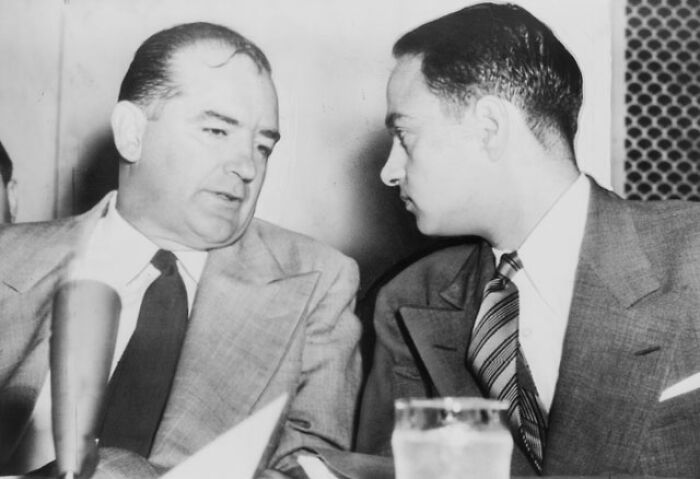 Two men in suits having a serious discussion, significant to decade-defining historical events, with a microphone in the foreground.