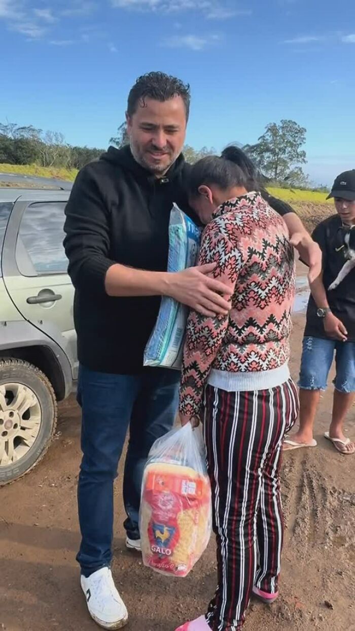 Man, known for feeding stray dogs, hugging a woman and holding a food bag near a car outdoors. Man, known for feeding stray dogs, hugging a woman and holding a food bag near a car outdoors.