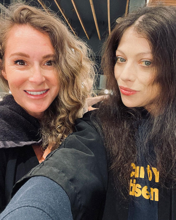 Two women smiling, one with curly hair, the other with straight hair, casually posing indoors. Two women smiling, one with curly hair, the other with straight hair, casually posing indoors.