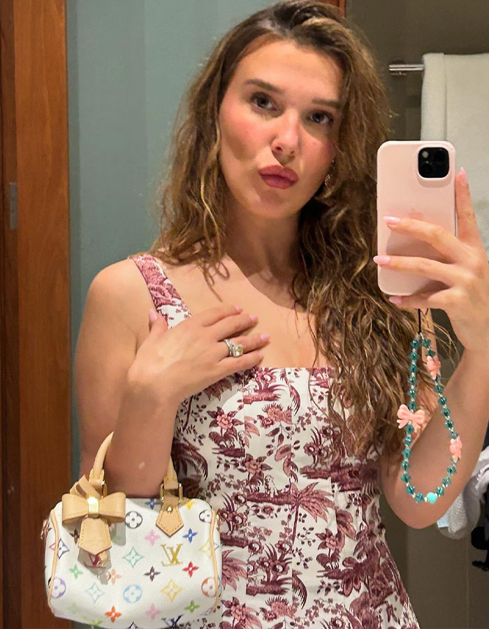 Woman taking a selfie, wearing a floral dress, holding a small Louis Vuitton handbag. Woman taking a selfie, wearing a floral dress, holding a small Louis Vuitton handbag.