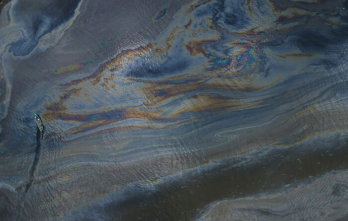 Aerial view of a lone boat in shimmering, oil-slick waters. Nature photography contest entry, showcasing environmental impact.