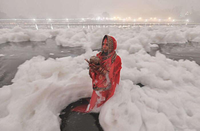 Person in red attire standing in foamy water, part of 2024 Nature "inFocus" photography contest.