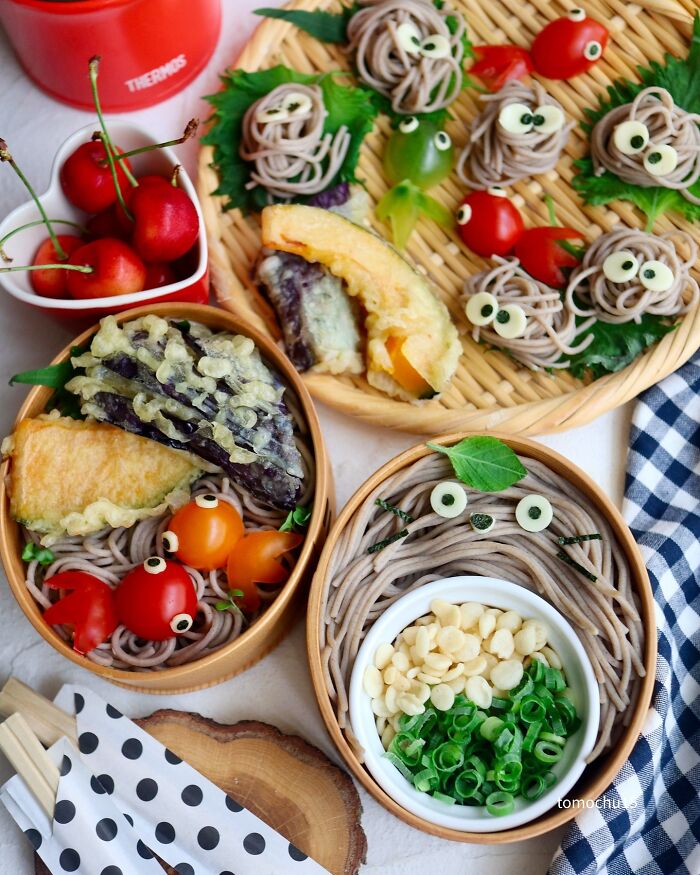 Creative lunchbox by a Japanese artist featuring noodles, tempura, and cherries in playful designs.
