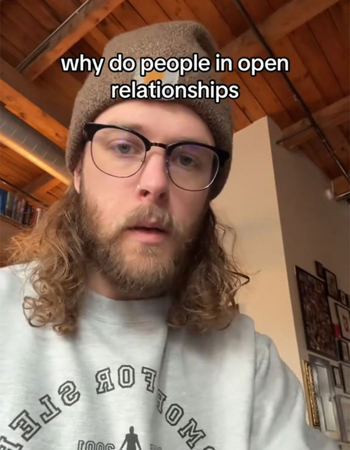 Man in an open relationship discussing perceptions while wearing a beanie and glasses in a cozy room setting. Man in an open relationship discussing perceptions while wearing a beanie and glasses in a cozy room setting.