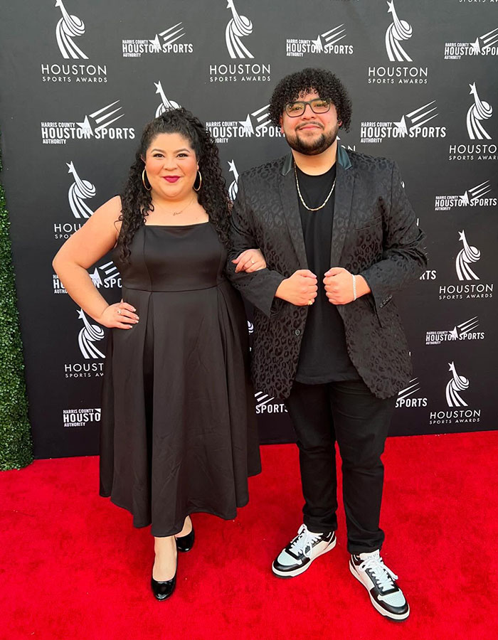 Red carpet appearance at Houston Sports Awards with two people, one in a black dress, the other in a patterned black jacket. Red carpet appearance at Houston Sports Awards with two people, one in a black dress, the other in a patterned black jacket.