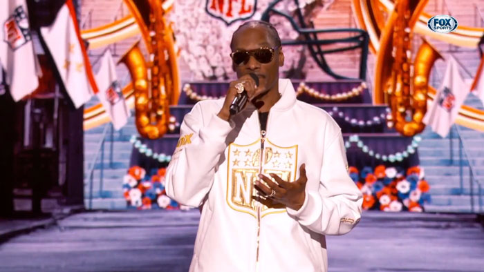 Snoop Dogg speaking on stage in a white NFL jacket, joking about an age gap, gaining viral attention. Snoop Dogg speaking on stage in a white NFL jacket, joking about an age gap, gaining viral attention.