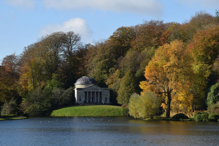 A small, classical building by a lake surrounded by autumn trees, exemplifying beautiful useless architecture.