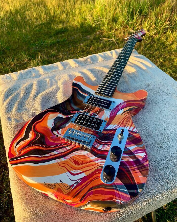 Colorful guitar crafted from unexpected materials, displayed outdoors on a towel.