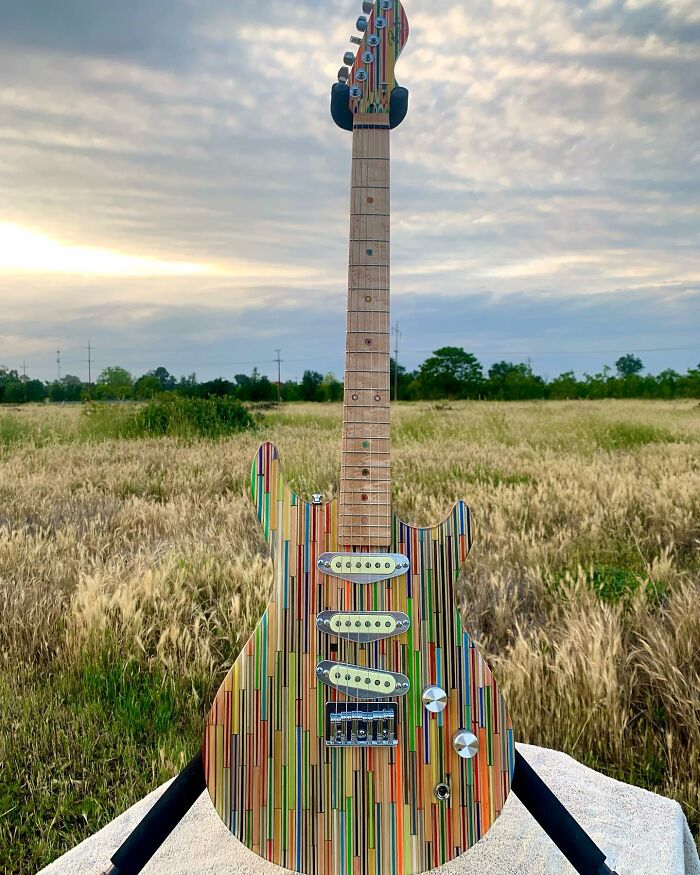 Stunning guitar made from unexpected materials, displayed outdoors against a field and cloudy sky backdrop.