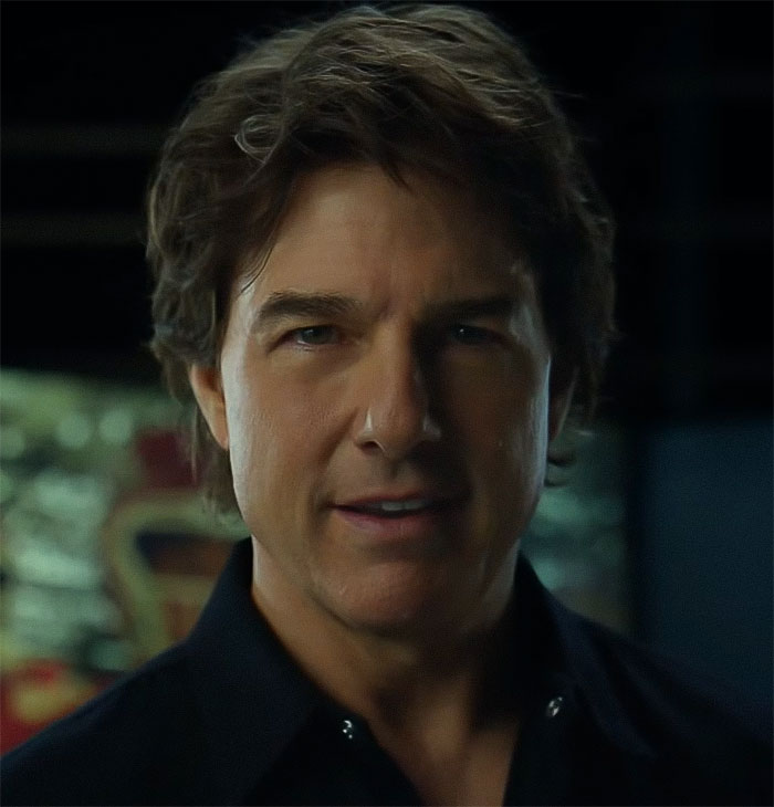 A man with dark hair and a black shirt inside, lighting focused on his face. A man with dark hair and a black shirt inside, lighting focused on his face.