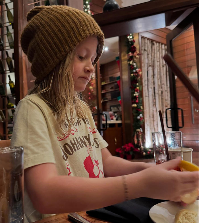 Child in a beanie and t-shirt seated at a table, possibly preparing a meal, with decorative background. Child in a beanie and t-shirt seated at a table, possibly preparing a meal, with decorative background.