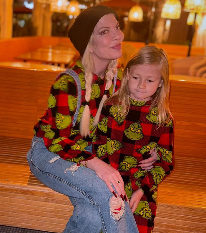 Woman in a knit hat and child in matching Grinch sweaters sitting on a wooden bench. Woman in a knit hat and child in matching Grinch sweaters sitting on a wooden bench.