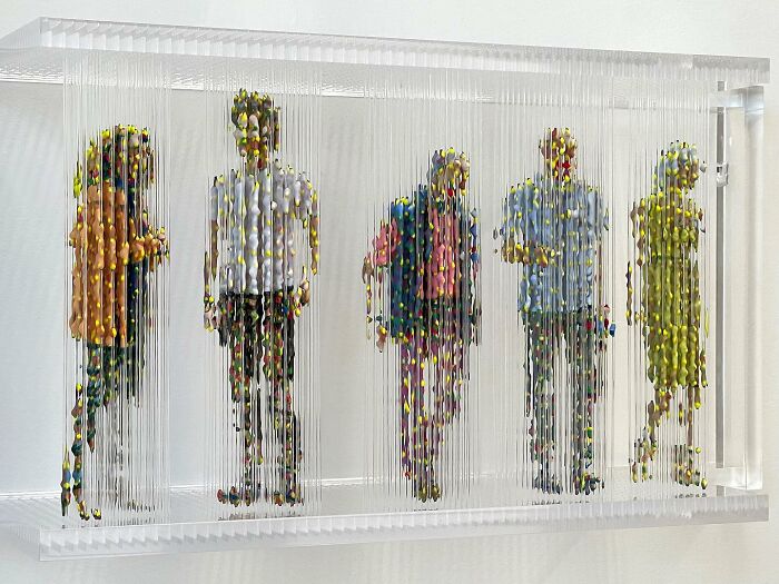 Fragmented three-dimensional paintings of people by Chris Dorosz, displayed in a transparent frame.