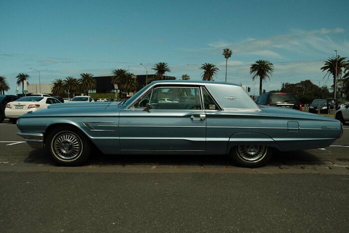 Vintage car parked on a street with palm trees in the background under a clear blue sky.