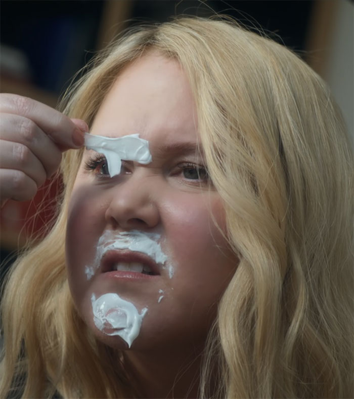 A woman with blonde hair making a funny face, removing cream from her face, in a comedic scene. A woman with blonde hair making a funny face, removing cream from her face, in a comedic scene.
