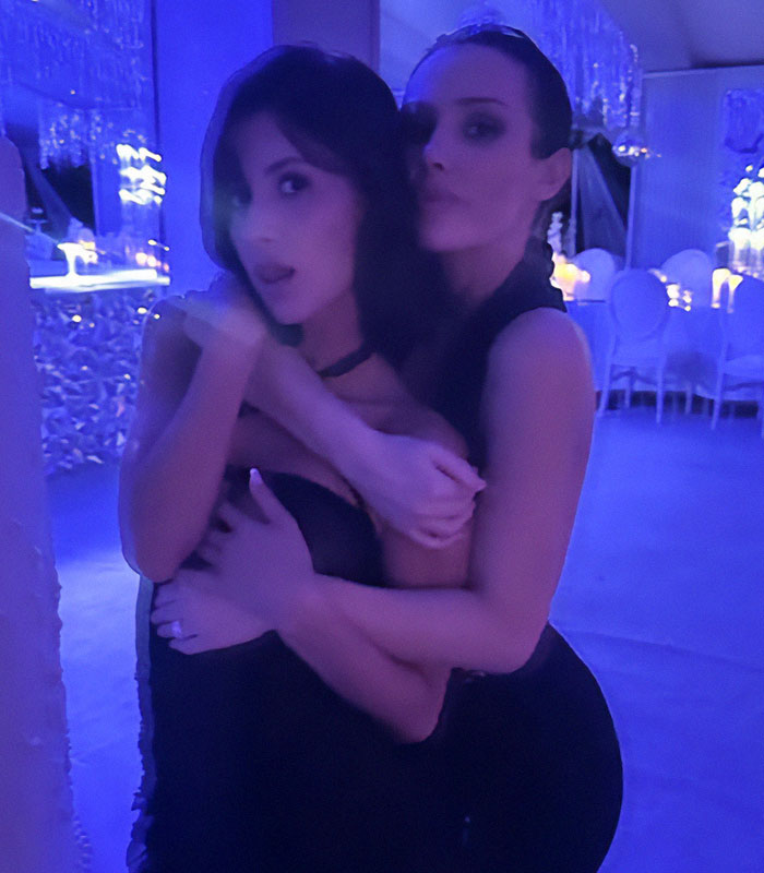 Two women in a dimly lit room, embracing at an event. Two women in a dimly lit room, embracing at an event.